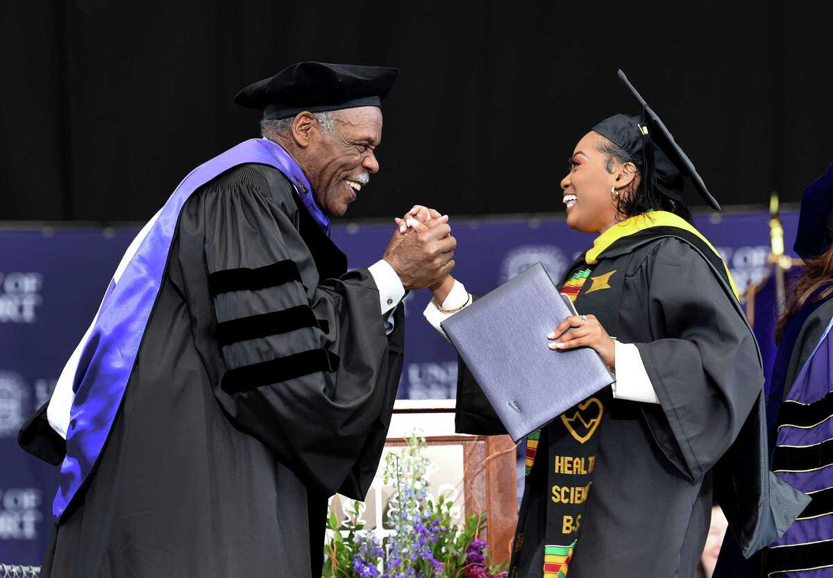 Above, Danny Glover, award-winning actor, producer and humanitarian, congratulates Hannan Yahya as she accepts her diploma. The University of Bridgeport held its commencement ceremony for undergraduate students Sunday at the Hartford HealthCare Amphitheater in Bridgeport. Glover was the keynote speaker. At right, Jenayia Patterson, of New Haven, shows her enthusiasm during the processional at the start of graduation.