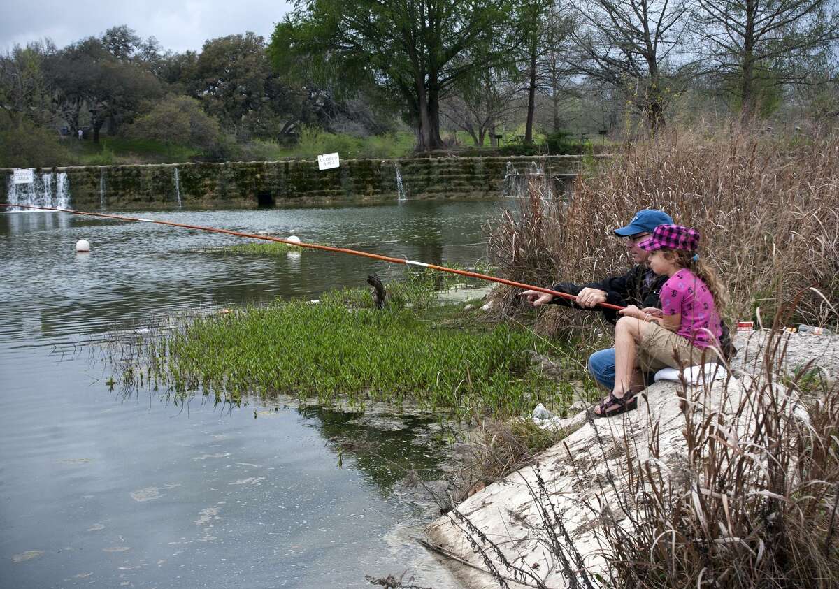 A young girl and her father fish in the river at Blanco State Park.