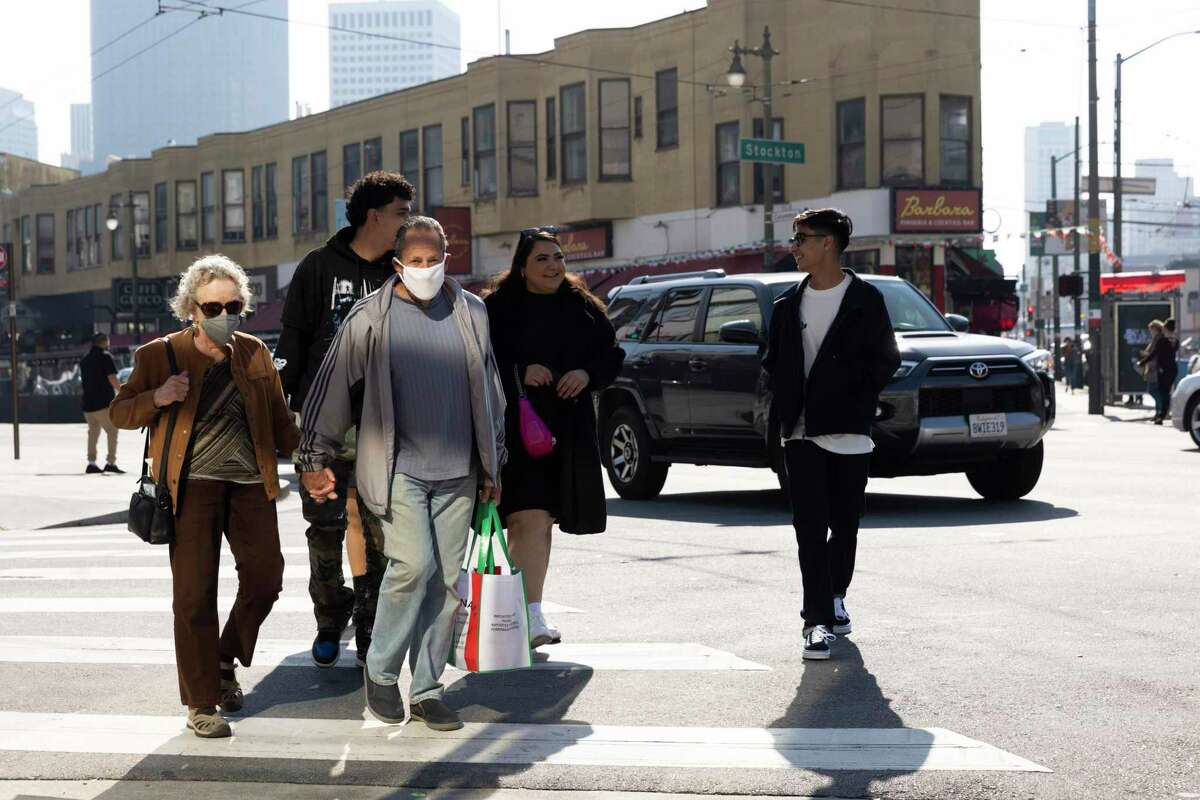 Pedestrians, some wearing masks and others not, walk along Columbus Avenue in the North Beach neighborhood of San Francisco in February.