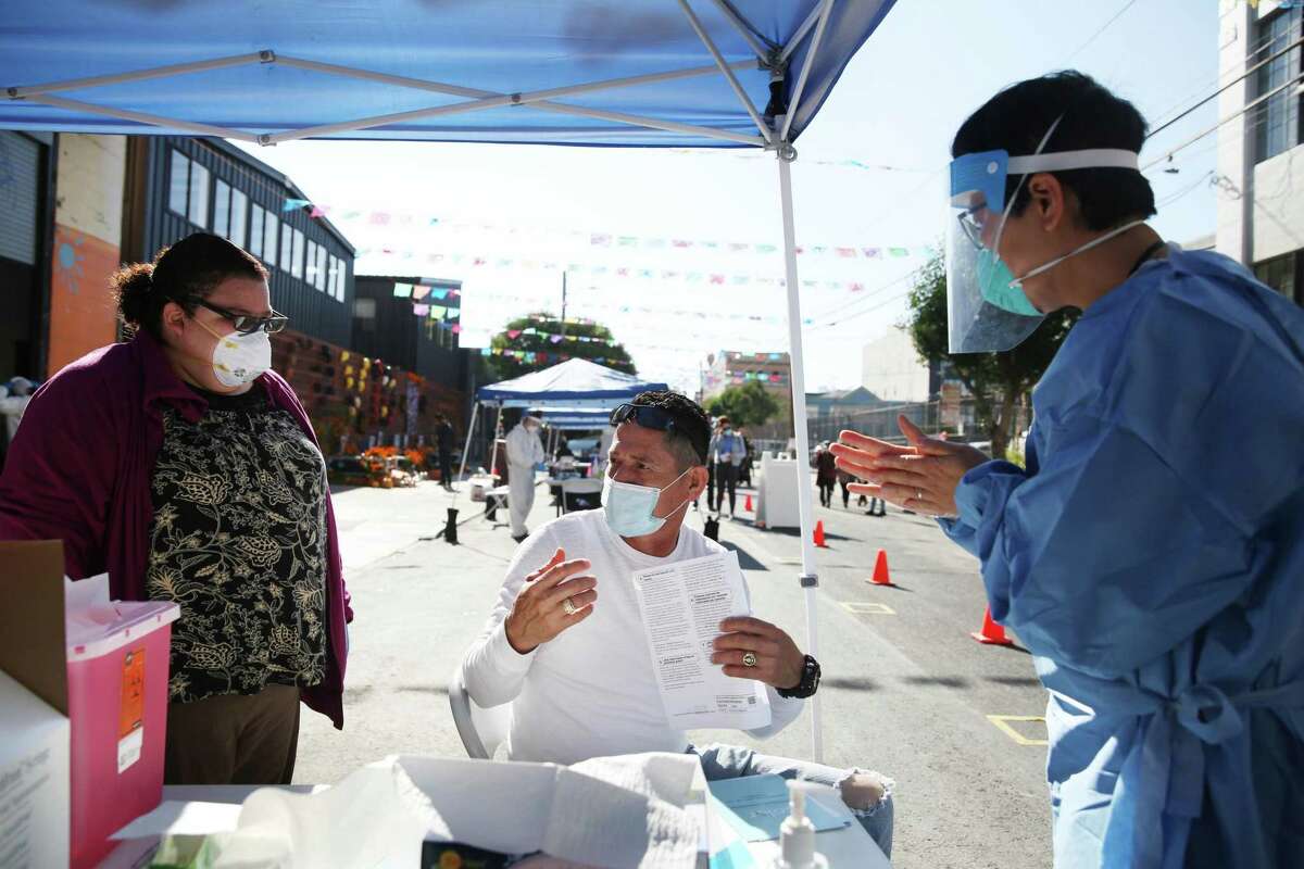 Po Lin Lui (right), Department of Public Health registered nurse, talks with Jose Rodriguez (center), of San Francisco, as Lorena Zavala (left), Department of Public Health administration support for the medical group, translates for them before Rodriguez gets a flu shot at the Latino Task Force Resource Hub on Thursday, November 5, 2020 in San Francisco, Calif.