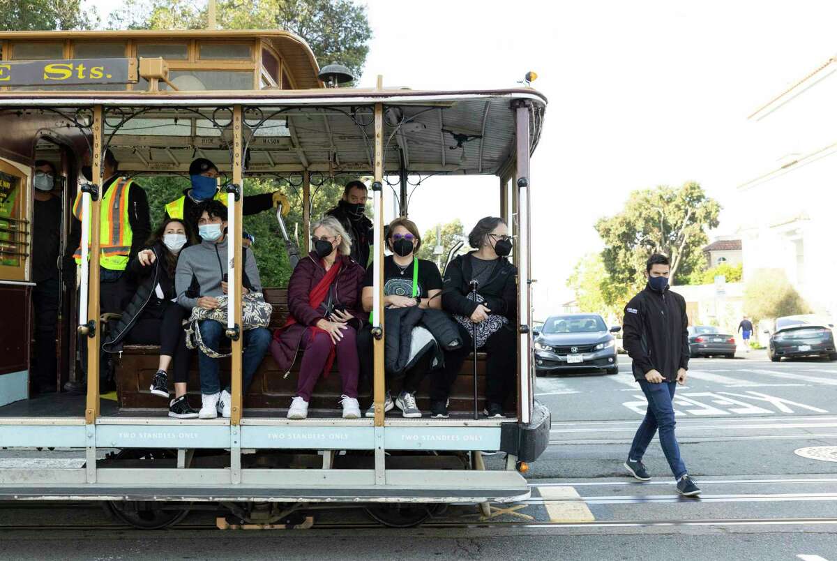 A cable car with passengers wearing masks stops at Lombard Street in San Francisco.