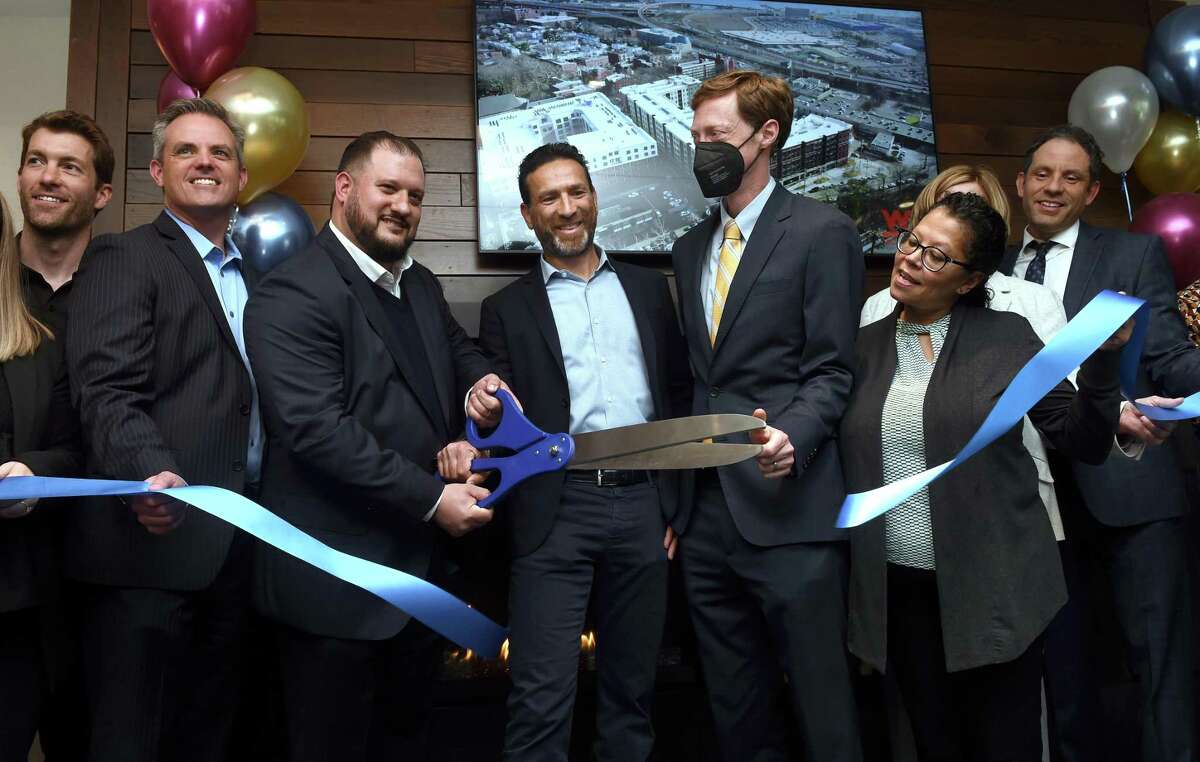 Darren Seid (holding scissors, left), owner and president of Epimoni, and Tomer Yogev, managing partner of Adam America Real Estate, cut a ribbon to ceremonially open the Olive & Wooster Apartments in New Haven Wednesday. From left are Josh Zucker, senior development manager for Adam America Real Estate; Garrett Sheehan, CEO of the Greater New Haven Chamber of Commerce; Seid; Yogev; Mayor Justin Elicker; Alder Carmen Rodriguez; Kozlowski (hidden), executive director of the Economic Development Corporation of New Haven; and Carlos Eyzaguirre, deputy economic development administrator for New Haven.