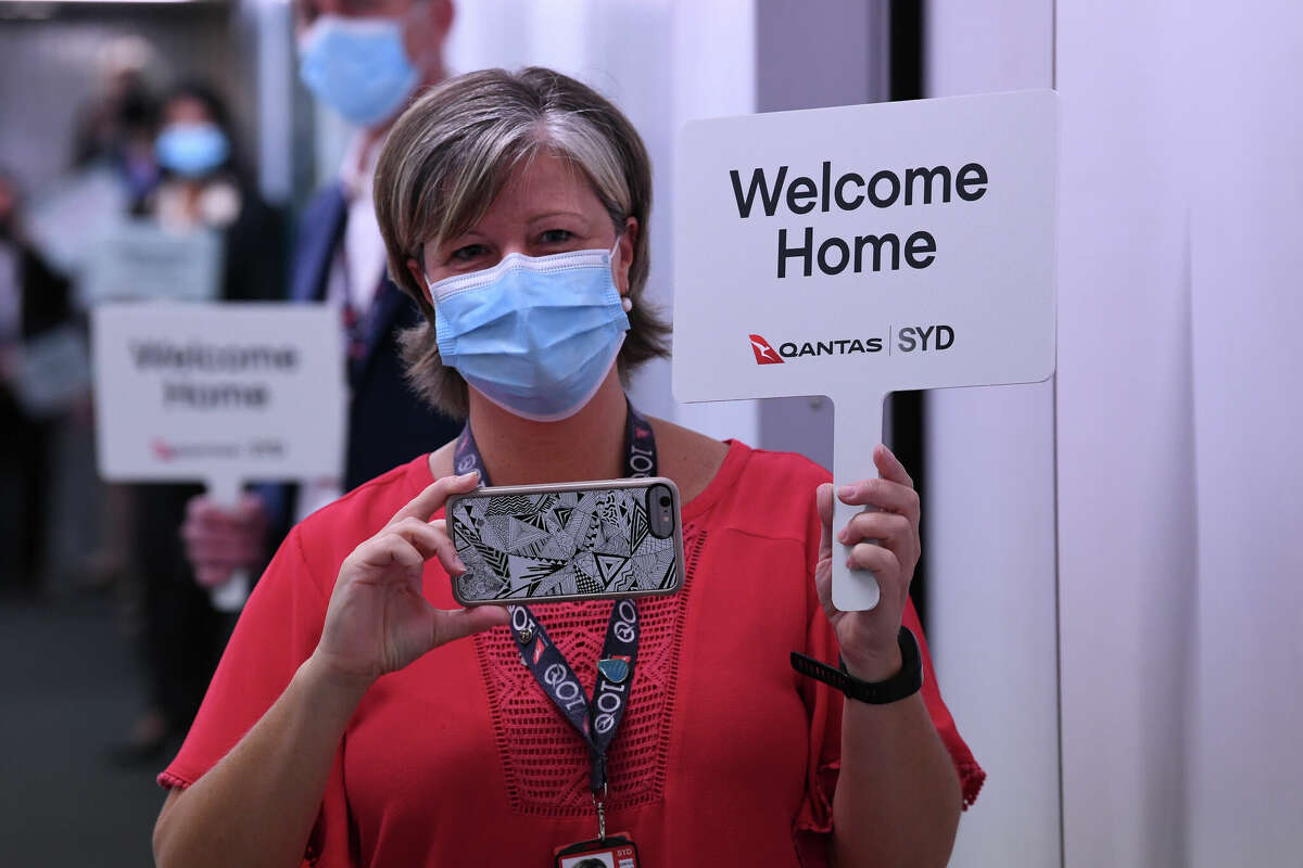 Qantas staff hold welcome home signs for arriving passengers off their flight from Los Angeles at Sydney Airport in November 2021.