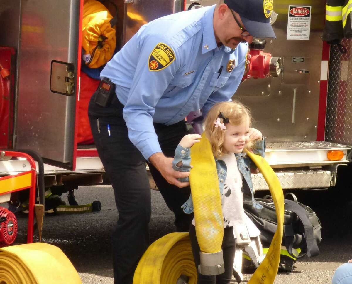 Manistee Fire Department Captain Chris Jeffries helps a young girl lift a fire hose at a Manistee County Library event on May 5. The department is also co-hosting the  Kid’s Safety Day and Cookout event in Manistee. 