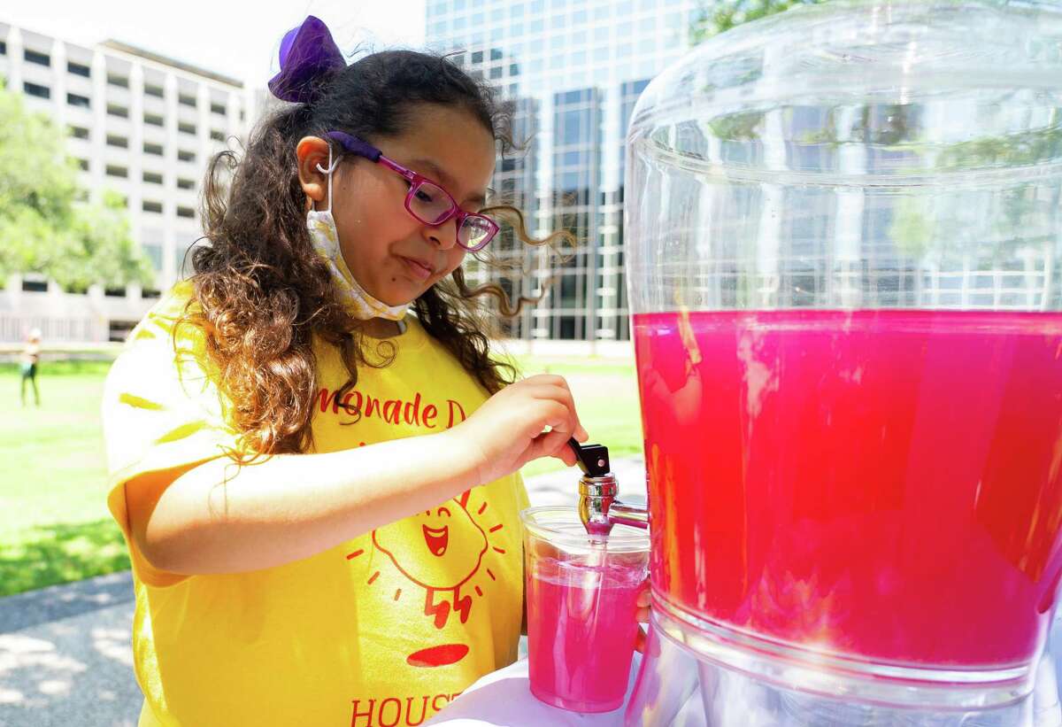 Eight-year-old Ariane Contreras fills a glass with her passion fruit flavored lemonade at her lemonade stand, Sunday, May 8, 2022, at the Williams Tower Waterwall in Houston.  Ariane heard about Lemonade Day, an organization that encourages young entrepreneurs, through a flyer at school and decided to have her first lemonade stand on Sunday.  She said she hopes to use the money she earns to buy a puppy, and maybe one day fund a trip to Disney Land.