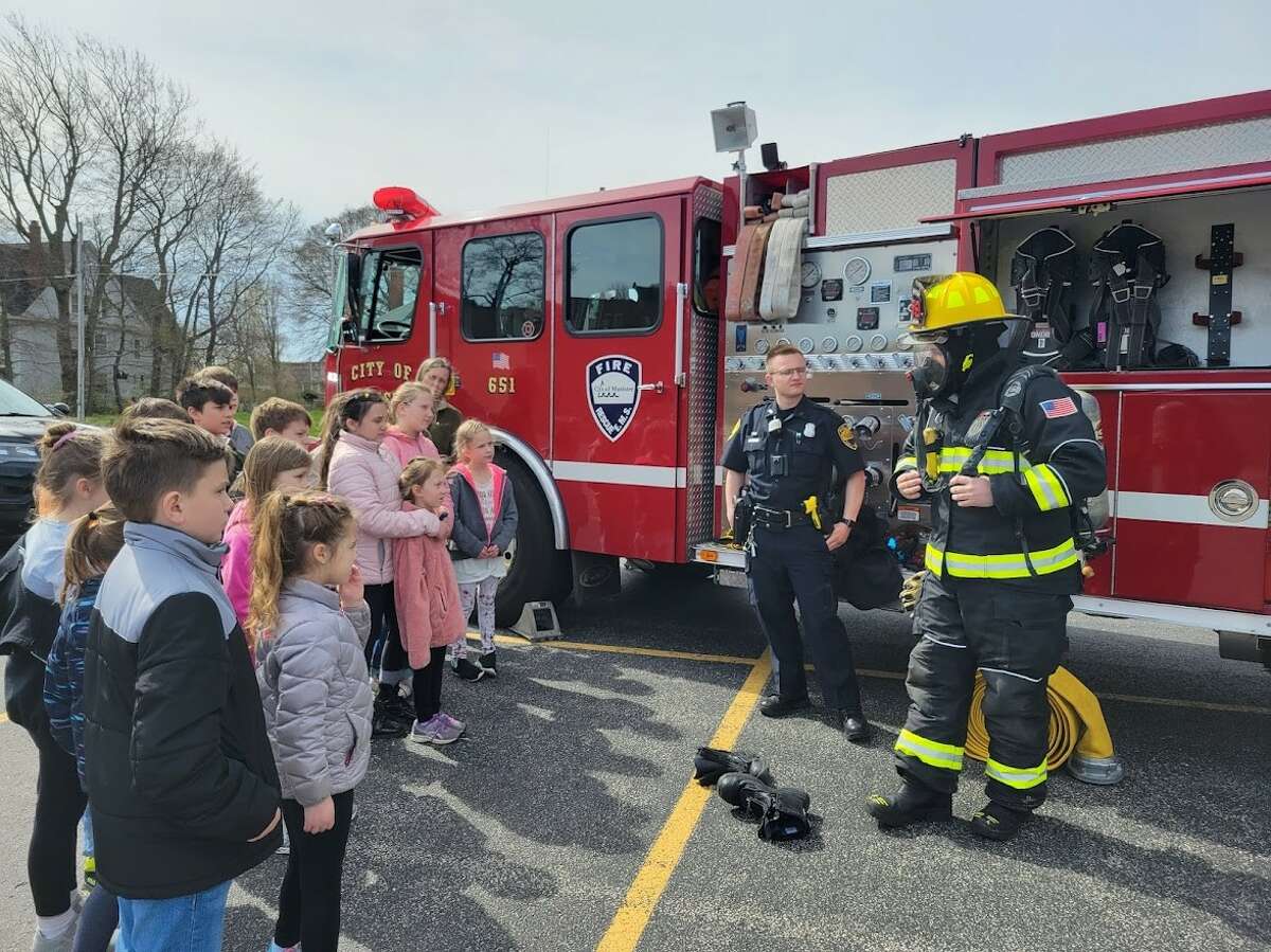 Brandon Nelson (right), Manistee City Fire Department firefighter/paramedic, shows his turnout gear to students Friday during a visit to Trinity Lutheran School.