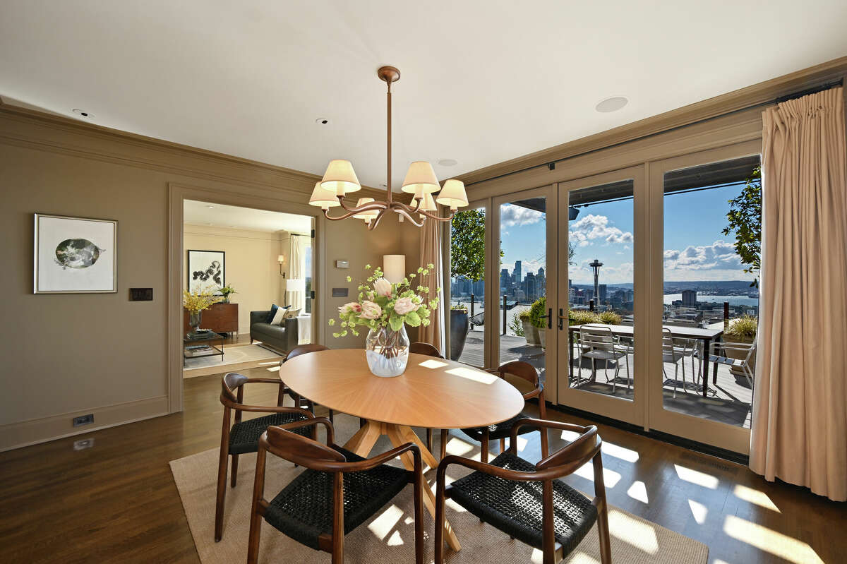 The dining room's glass doors open to the sun-soaked deck and city skyline. 