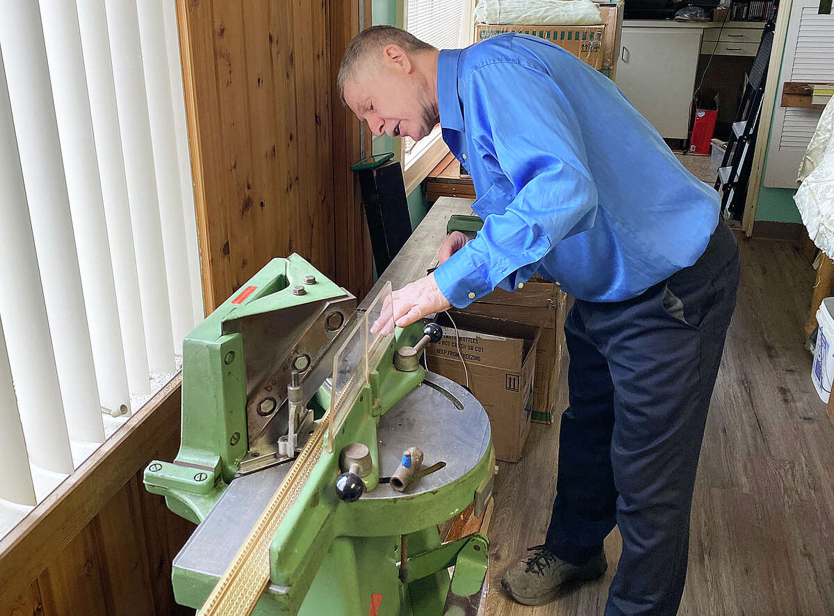 Will Lee recently opened "The Framing Guy" shop, along with his wife Anne, under the water tower on M-142 in Elkton. Above, Lee uses a machine to cut pieces of ornate wood into smaller pieces for a frame.