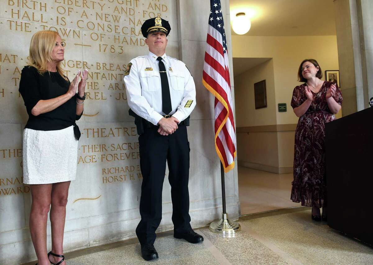 Timothy Wydra, center, sworn in as deputy chief of the Hamden Police Department, is applauded by his wife, Mary, left, and Mayor Lauren Garrett at Memorial Town Hall Wednesday.