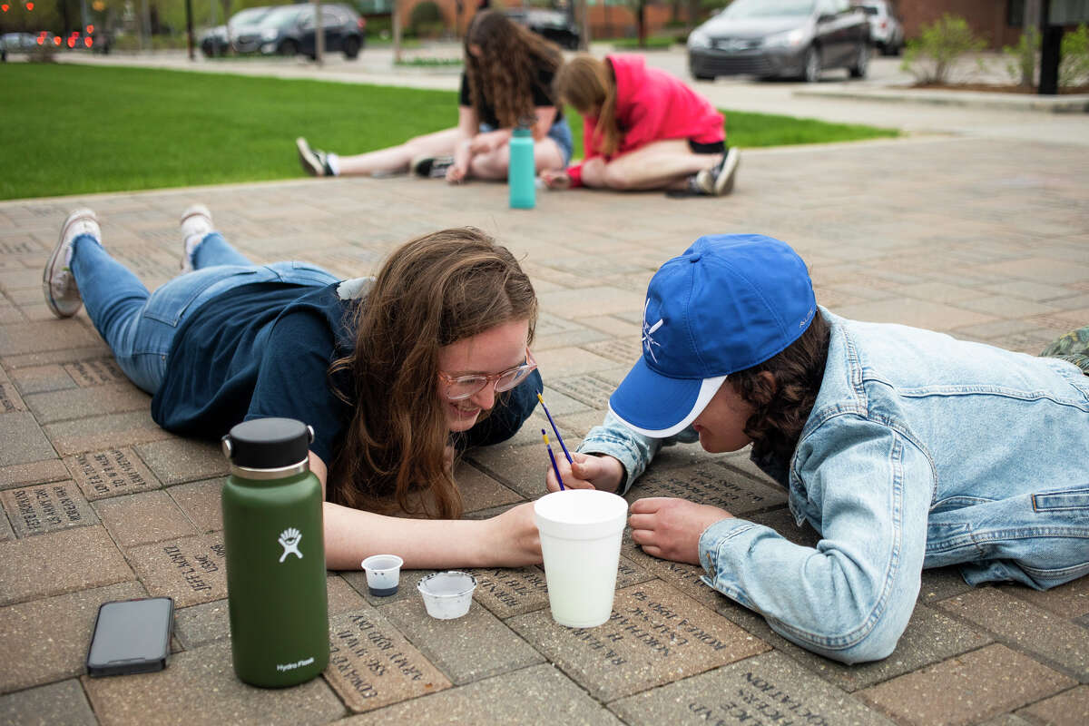Dow High juniors Paige Dolph, left, and Clara Allington, right, touch up the paint on veterans' names at the Midland Veterans Memorial alongside their classmates Wednesday, May 11, 2022 in downtown Midland.