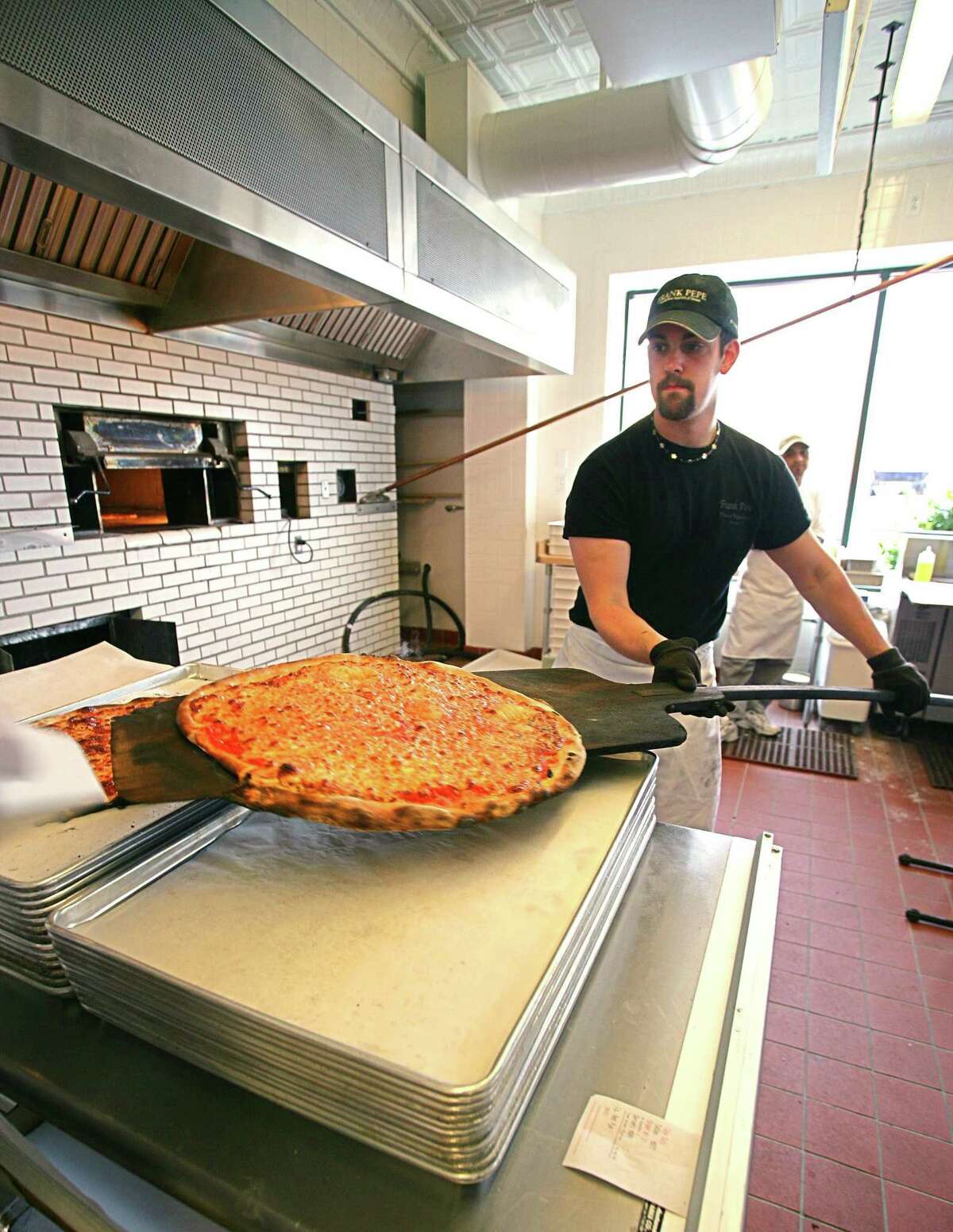 Oven Man Ryan Hills uses a piel to take a pie out of the oven at Pepe's Fairfield during the grand opening in 2006.