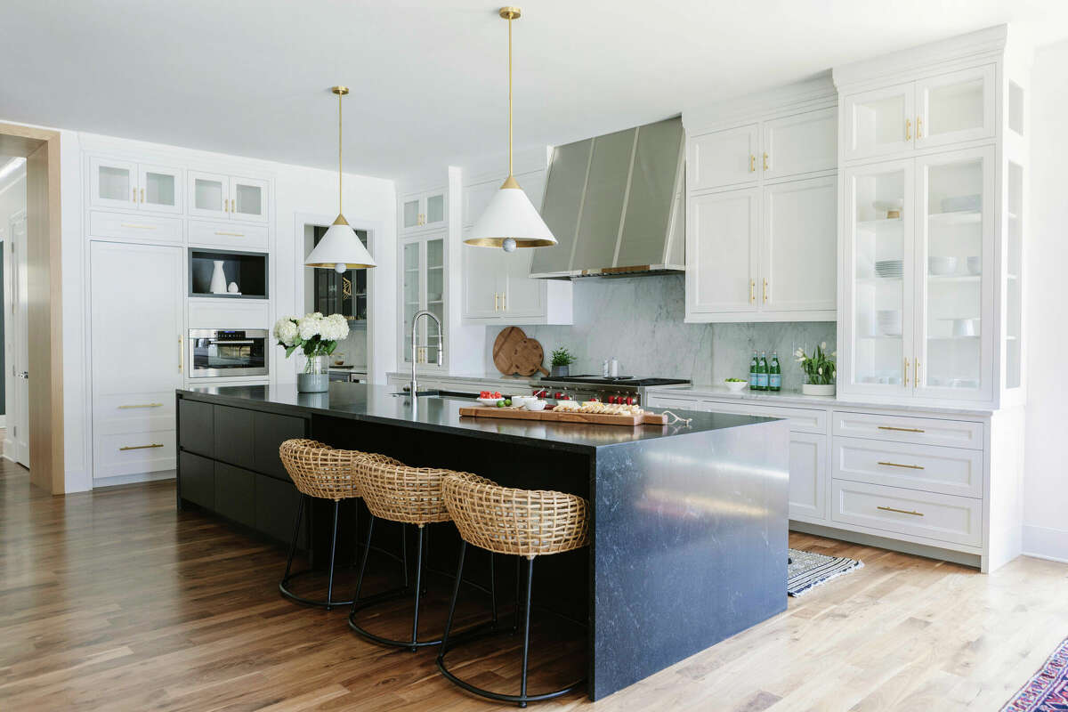 This kitchen design has woven Palecek kitchen stools and a striking midnight blue stone island to balance the extensive Shaker-style white and glass cabinetry.
