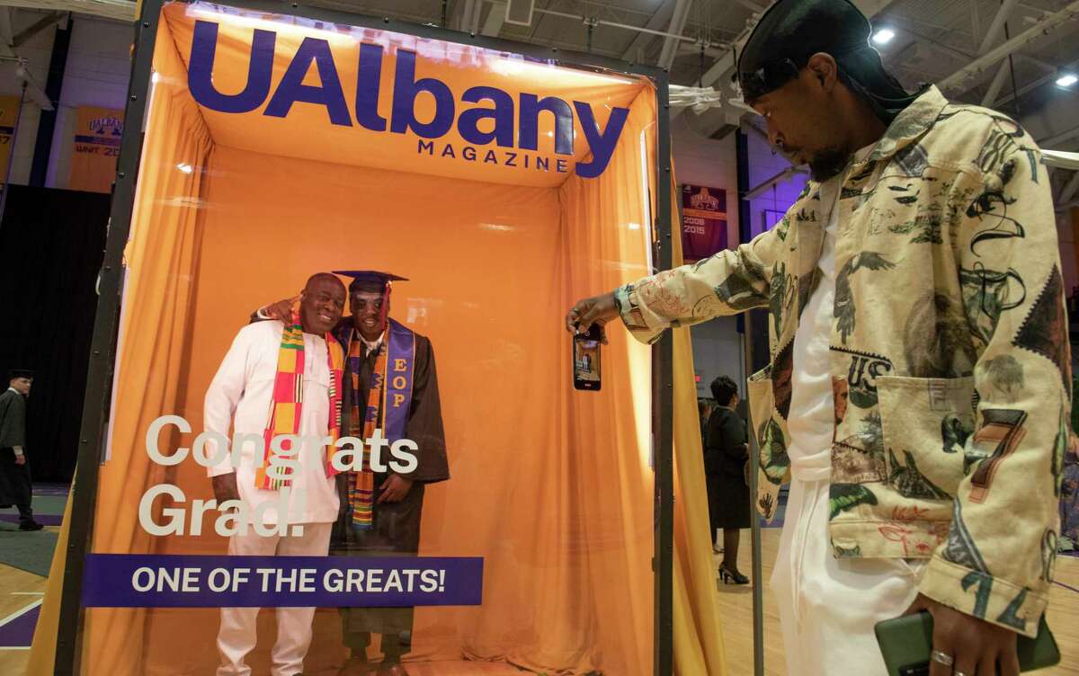 University at Albany graduate Joshua Asamoah of the Bronx and his father Edwin Asamoah get their photo taken in a booth by Joshua’s brother Desmond Osei after his stage crossing ceremony at SEFCU Arena on Thursday, May 12, 2022 in Albany, N.Y. UAlbany is once again offering the smaller gatherings to allow graduates to celebrate to address concerns about being in a large gathering during a COVID-19 surge.