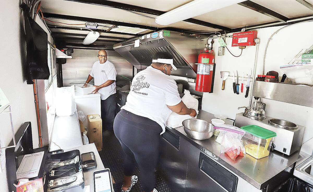 John Badman|The Telegraph Andrew Thompson, left, works inside his food truck called Homestyle Grill BBQ on the opening day of the Flock food truck park in Alton. A county board committee this week expressed opposition to lowering permit fees for food trucks.