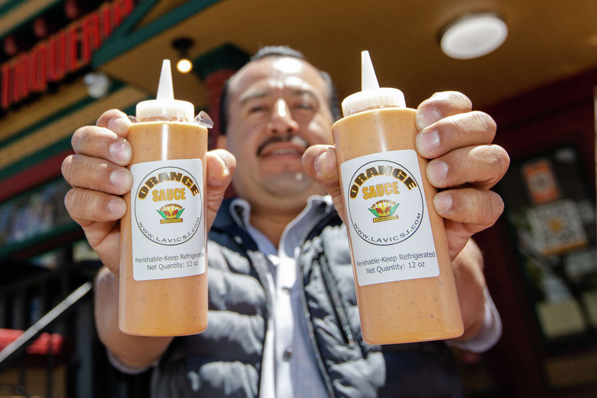 La Victoria Taqueria operations manager Nick Barrita holds bottles of the restaurant's signature orange sauce outside its downtown location in San Jose, Calif., on May 10, 2022.
