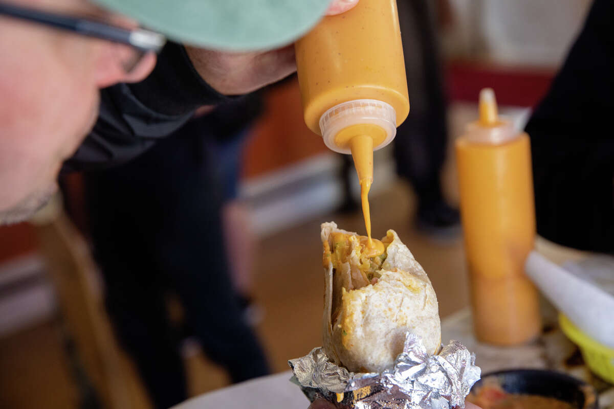 El cliente Ryan Damm vierte la salsa de naranja exclusiva de La Victoria Taqueria en su burrito en un restaurante en San José, California, el 10 de mayo de 2022.