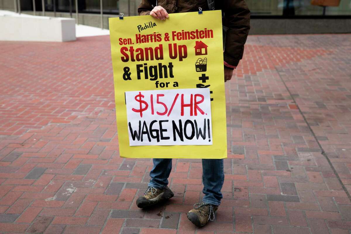 A demonstrator with the Poor People’s Campaign carries a sign in front of Sen. Dianne Feinstein’s office in San Francisco during a February 2021 rally to support federal legislation that would end the subminimum wage for tipped workers and raise the minimum wage to $15 per hour.