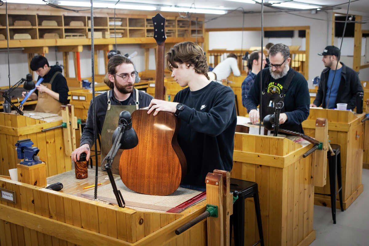 Instructor Cooper Wentz, center, chats with Kyle Winter of Big Rapids, left, a student of the Galloup School of Guitar Building and Repair Tuesday, April 19, 2022 in Big Rapids.
