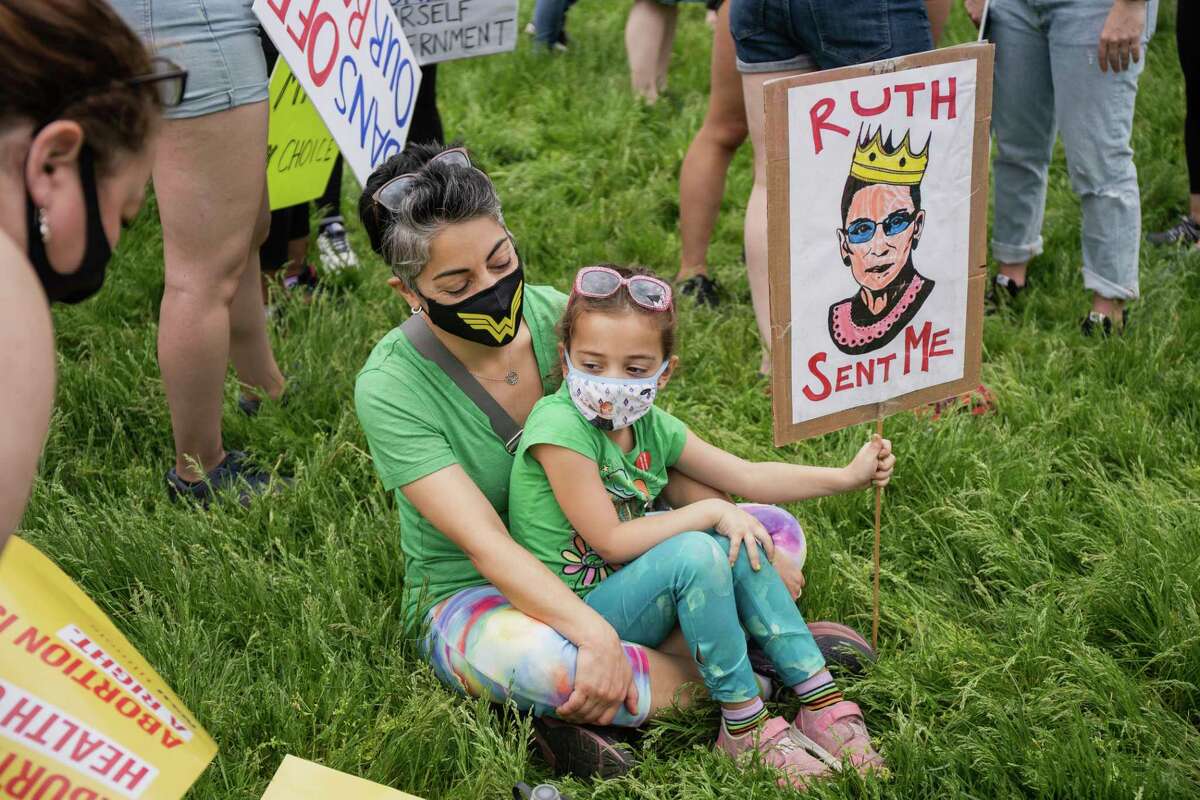 Maryam and Riley Brotine sit on the grass while holding a Ruth Bader Ginsburg during a protest Saturday morning, May 14, 2022. Demonstrators are rallying from coast to coast in the face of an anticipated Supreme Court decision that could overturn women’s right to an abortion. (Pat Nabong /Chicago Sun-Times via AP)