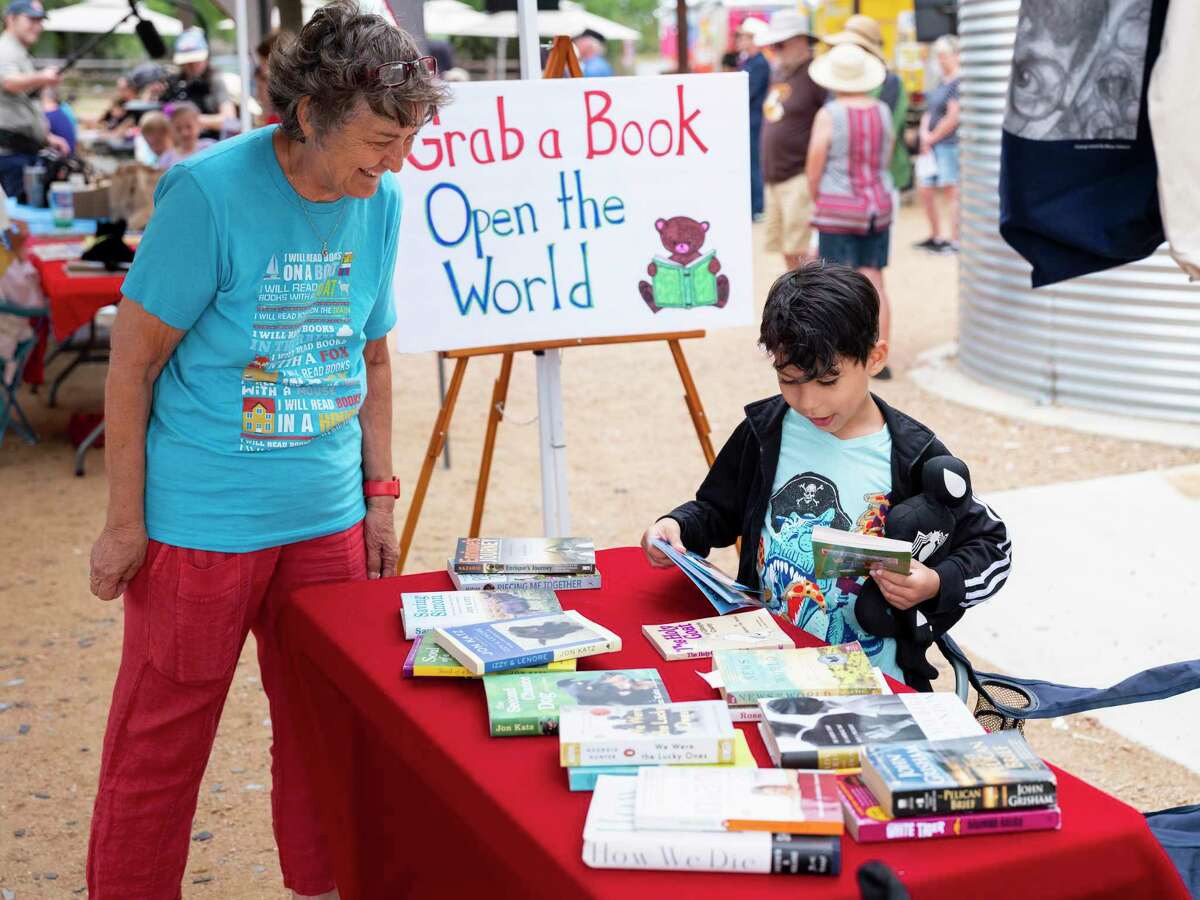 Carol Wichman, a retired school librarian from Ohio, left, encourages Elias Valenzuela, a 2nd grader, to choose his favorite books from her booth during a celebration of books event in Fredericksburg, on Saturday, May 14, 2022. Recently Fredericksburg ISD removed books from their library shelves for various content which opponents say is paramount to banning authors’ voices from their children at school.