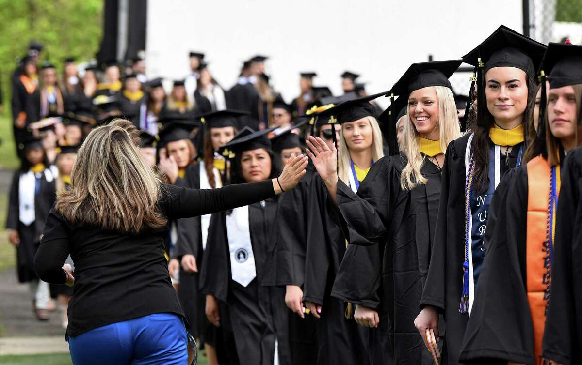 Christine Valle, left, reaches to high-five her friend Kaley Langlois during the procession at the start of Western Connecticut State University’s commencement exercises Sunday, May 15, 2022 at the Macricostas School of Arts & Sciences.