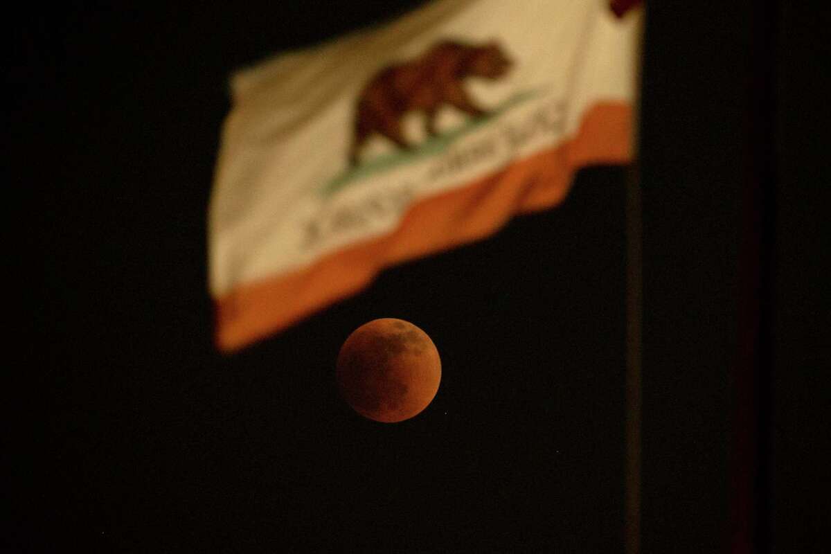 A total lunar eclipse is seen behind a California State flag, in El Monte, Calif., Sunday, May 15, 2022.