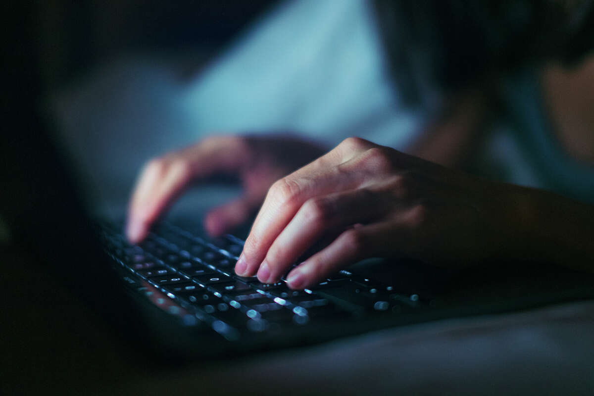 Close-up shot of female hands typing on computer keyboard, lying on bed, working late at home.