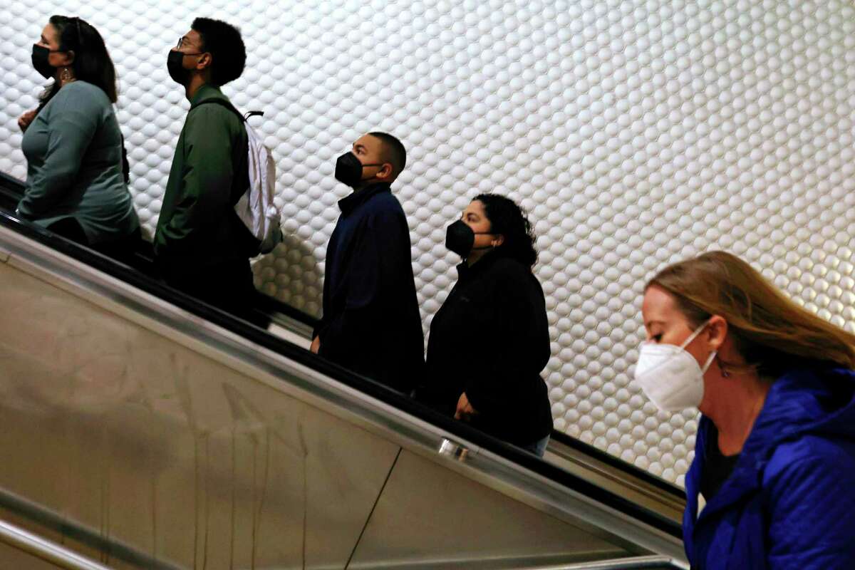 Lidé v maskách jezdí na eskalátoru a vystupují po schodech z nástupiště na stanici BART Powell Street v úterý 19. dubna 2022 v San Franciscu v Kalifornii.  Policistům BART bylo řečeno, aby neprosazovali mandát přepravní agentury v podobě masky, podle osoby obeznámené se záležitostí, která nebyla oprávněna veřejně mluvit jménem BART.