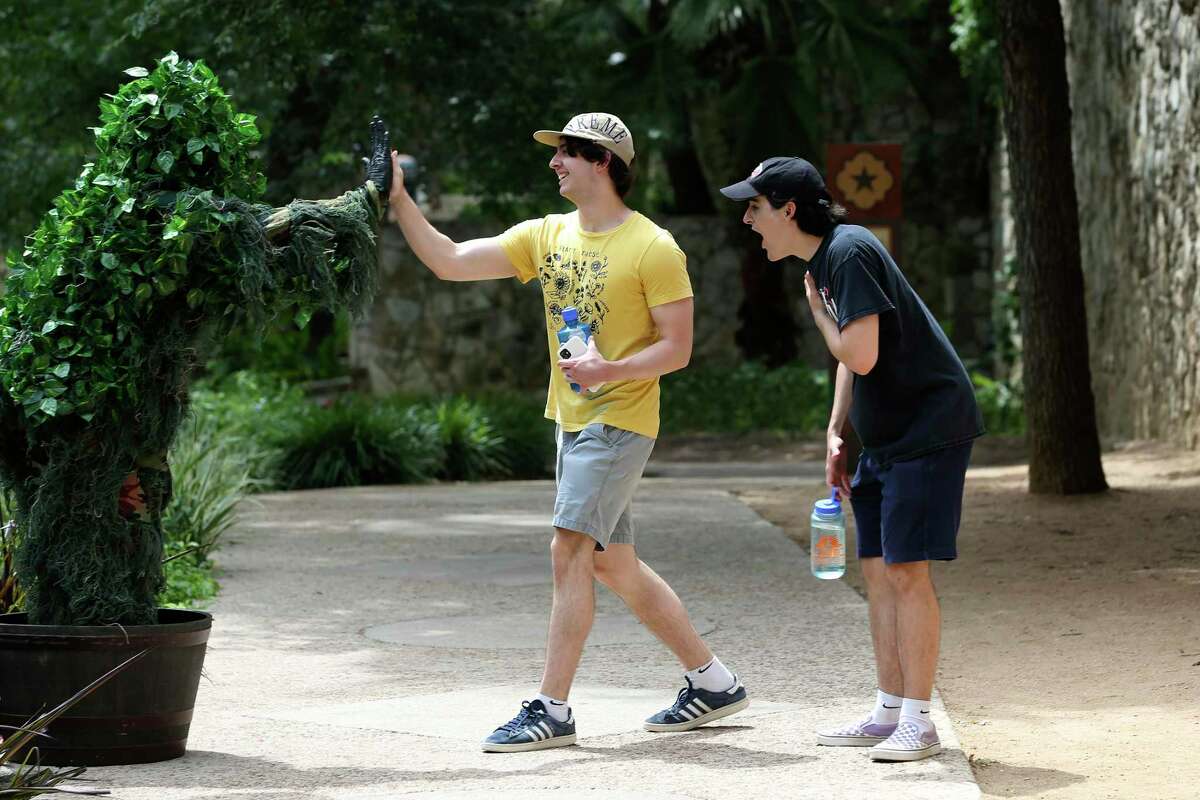 James Lea, center, and Nico Gonima, right, share a post-scare high-five with Joe Jones, aka the Texas Bushman, on the River Walk. Jones covers himself in fake ivy and squats inside a planter to scare passersby, then posts videos of their reactions on YouTube and social media.