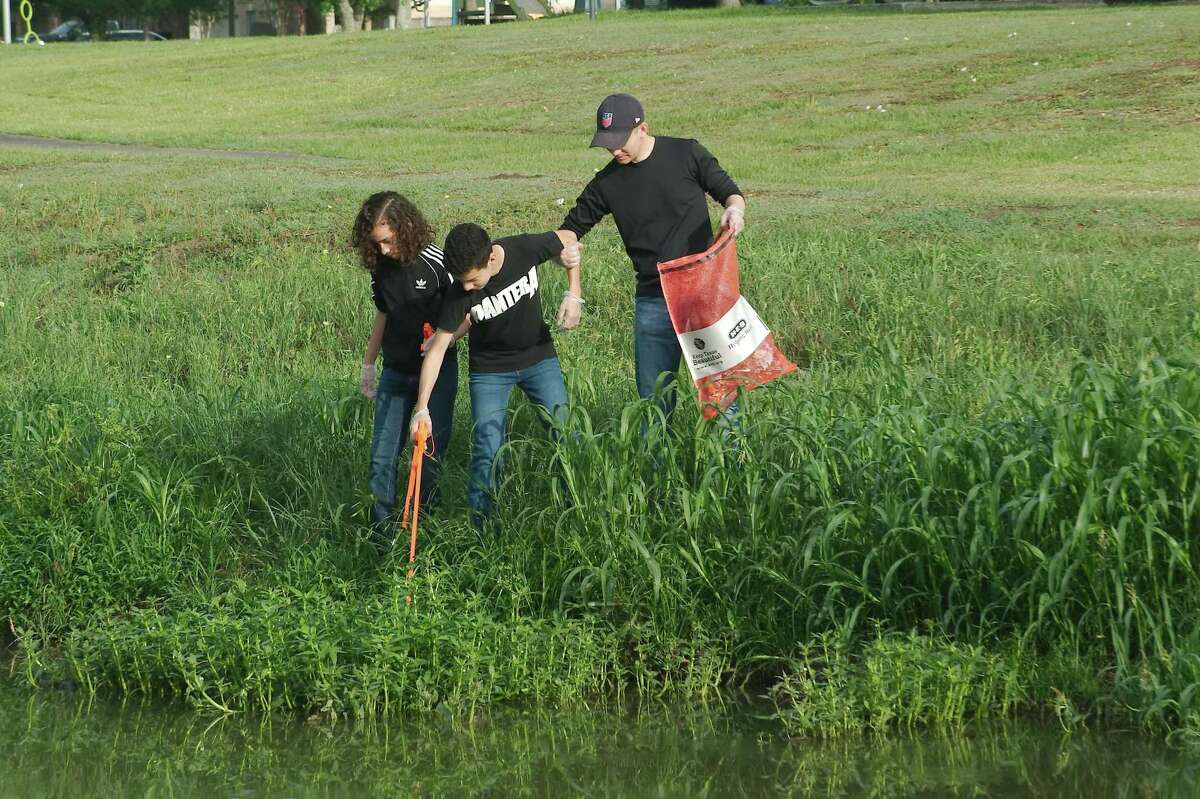 Diego James looks for trash while brother Joaquim gets help from their father, Matthew, along a slippery bank as they pick up trash along Mary's Creek at Centennial Park in Pearland during Keep Pearland Beautiful’s Waterways Cleanup event on May 7.