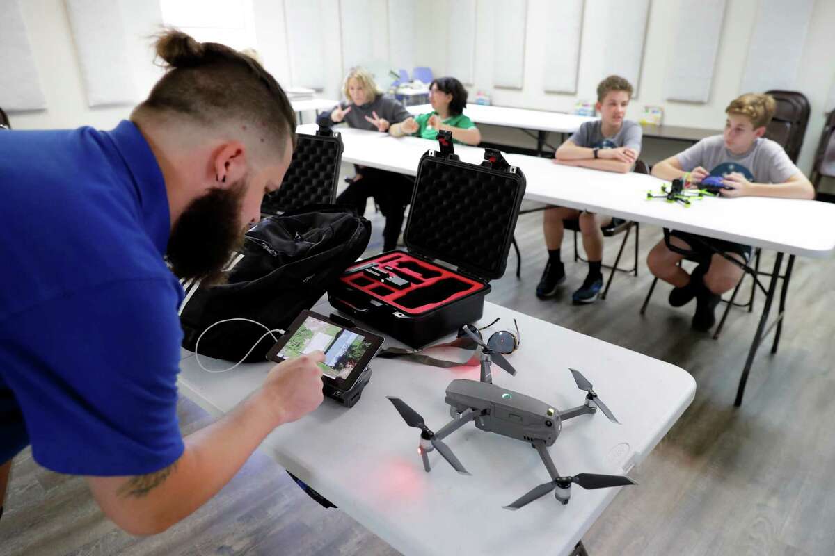 Josh Beatty, left, with Aha Education LLC, scrolls through photos taken by a dront, right, as students wait in the background as part of the drone education program for students at the private All Nations Community School Tuesday, May 17, 2022 in Oak Ridge, TX.