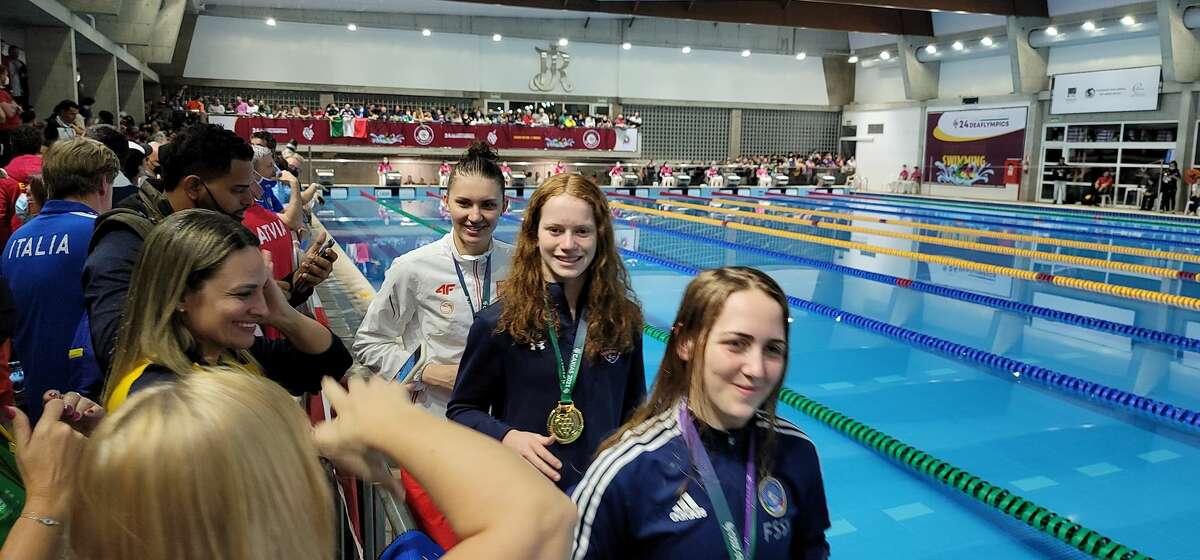 Carli Cronk, center, walks past the international competitors as she displays the gold medal she won in the 400-meter freestyle at Summer Deaflympics swimming competition held May 2-9 in Caxias do Sul, Brazil. 