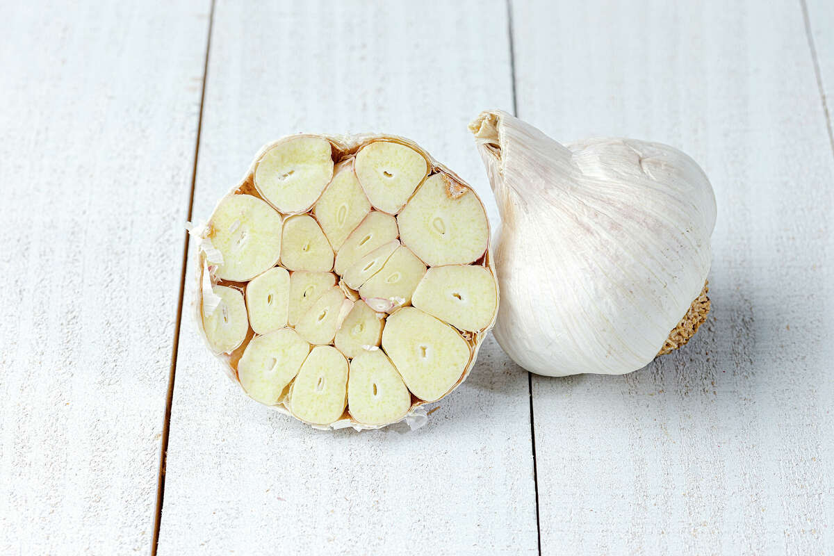 One whole garlic head and one head of garlic cut in half on wooden surface