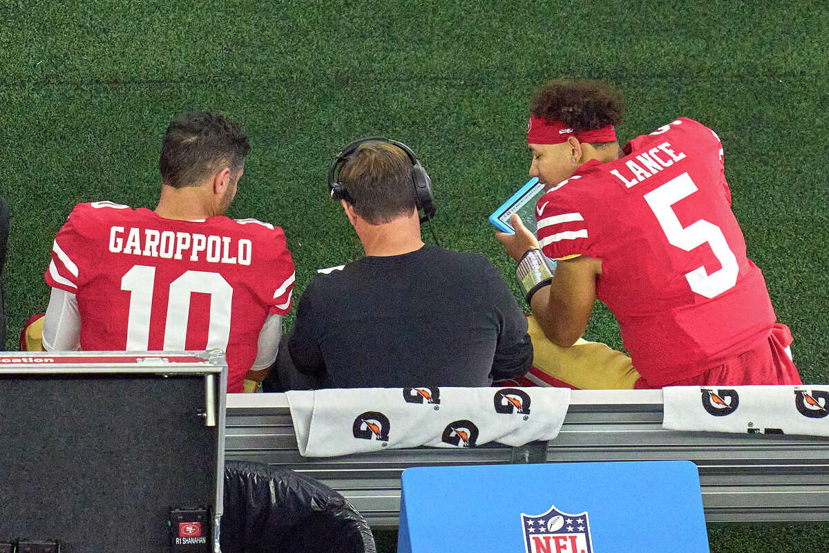 San Francisco 49ers quarterbacks Jimmy Garoppolo and Trey Lance look over their Microsoft Surface tablets with San Francisco 49ers quarterbacks coach Rich Scangarello during the NFC wild-card game between the San Francisco 49ers and the Dallas Cowboys on Jan. 16 at AT&T Stadium in Arlington, Texas.