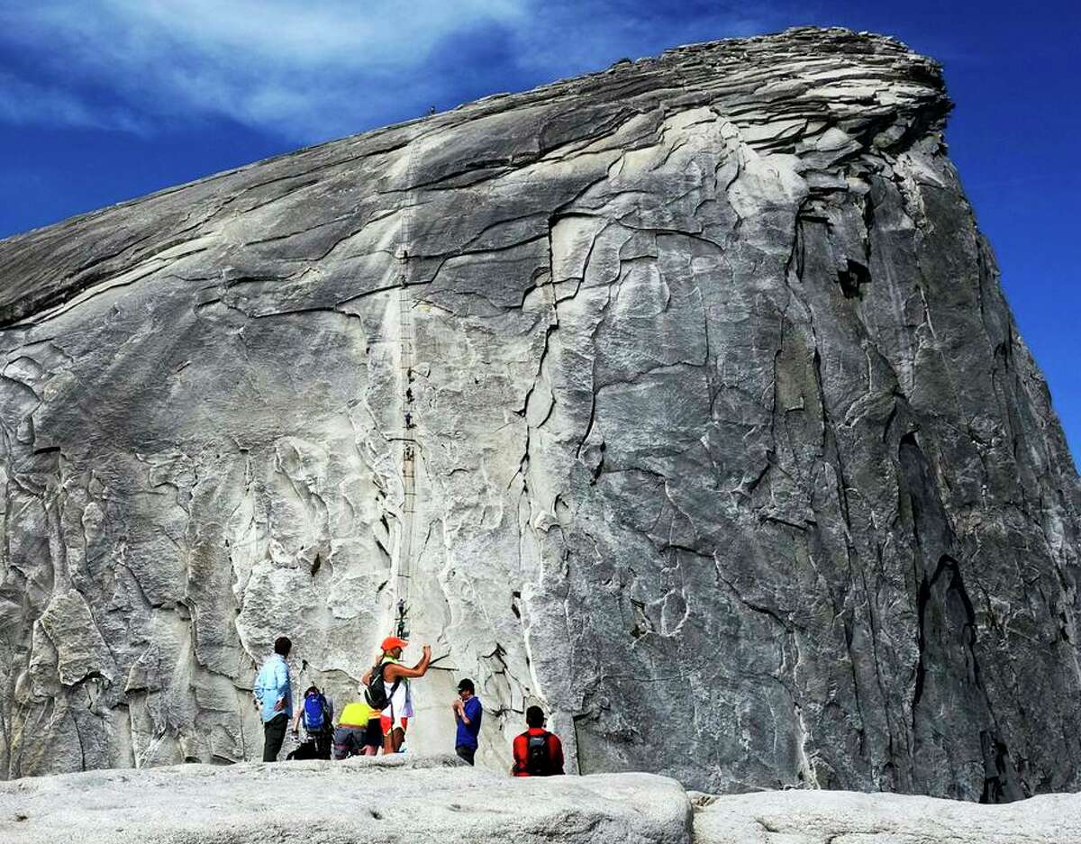 In this July 15, 2014 photo, hikers gather in the foreground as climbers use the assistance of cables to scale Half Dome in Yosemite National Park National Park in California's Sierra Nevada.