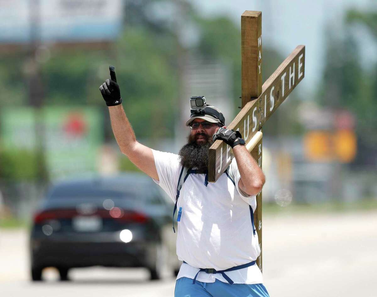 Josh Duncan with Walking The Cross Ministries gives thanks to God while carrying an eight-foot-tall, 60-pound wooden cross along FM 1488, Tuesday, May 10, 2022, in Magnolia. Every day, Duncan makes the four-hour trek from I-45 to F.M. 2948. At first, he made the route once or twice a month, but he said God called him into ministry, so he quit his job and started his ministry. "With everything going on in the world right now, people are looking for answers," he said. "I want to be a physical witness to Him for those who see me."
