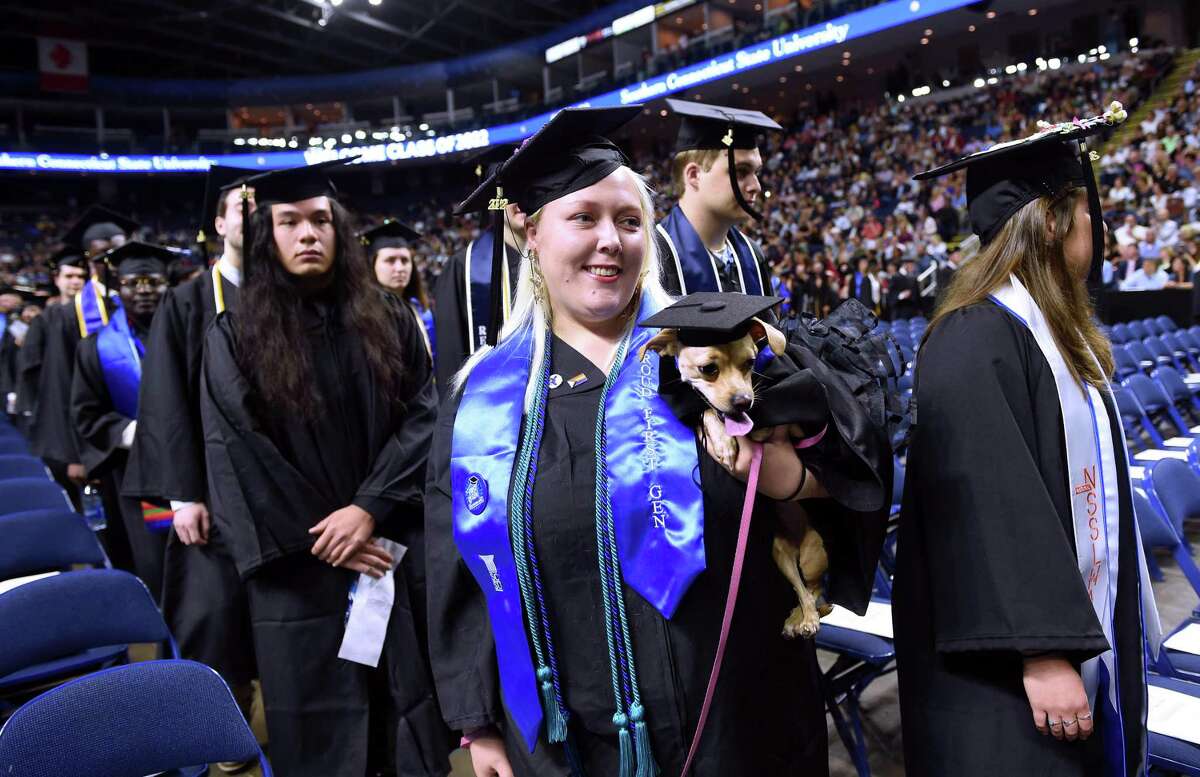Nicole Coffey carries her service chihuahua, Monroe, into the Southern Connecticut State University commencement at the Total Mortgage Arena in Bridgeport on May 20, 2022.