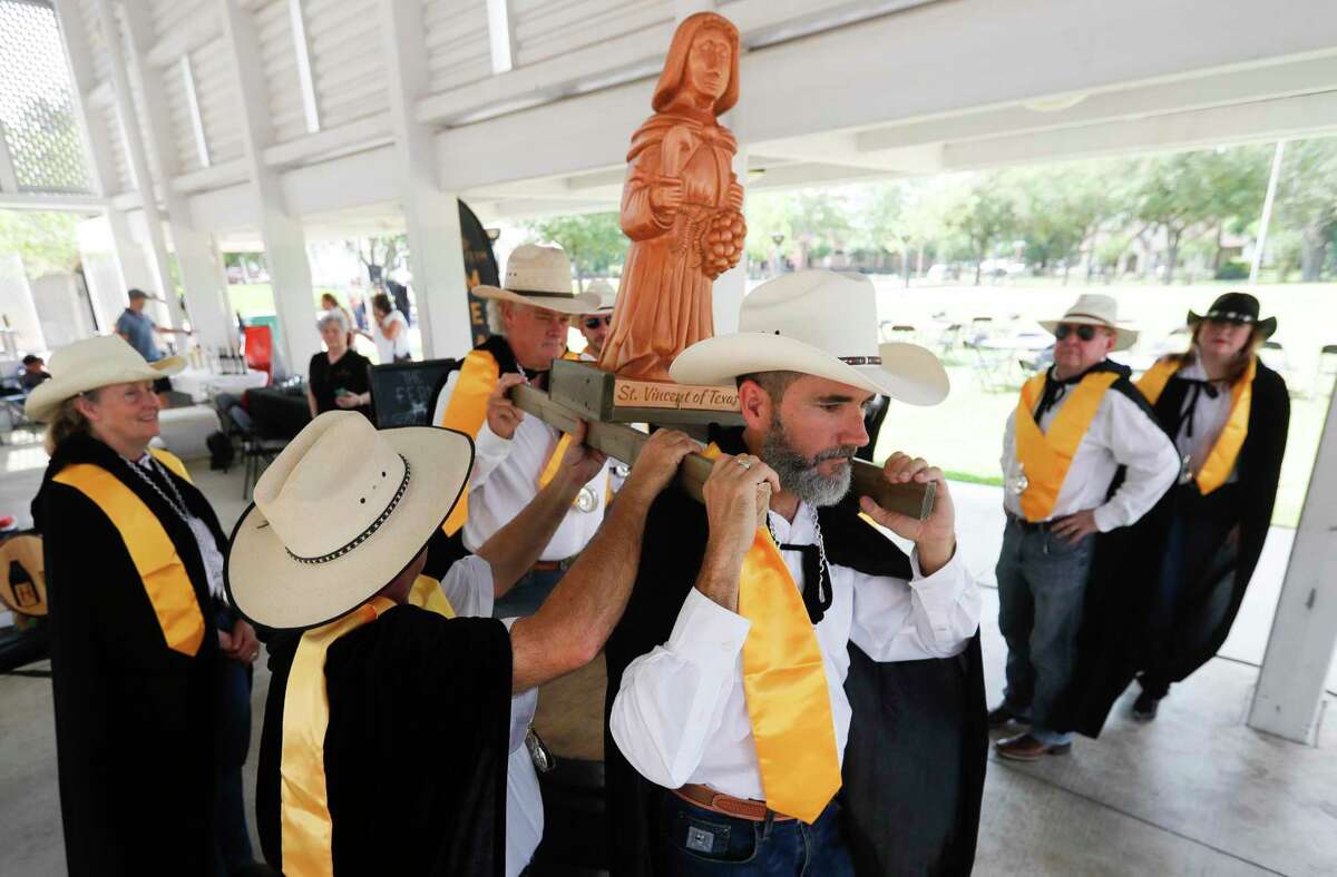 Dressed vendors carry a wooden sculpture of Saint Vincent, patron saint of winemakers, dressed in French winemaking attire with a Texan twist during the blessing of wine at Heritage Place Park on Saturday in Conroe.  The event celebrated Saint Vincent, who discovered the art of pruning vines for better production after his donkey ate several vines.  On the left, Philippe Legrand, on the left, shows Van Brackin how to control the quality of wine.