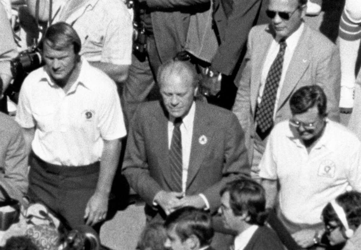 10/09/1976 - Texas Longhorns v Oklahoma Sooners. President Gerald Ford, center, is escorted out to the middle of the Cotton Bowl field for the pre-game coin toss by Sooners head coach Barry Switzer, left, and Longhorns head coach Darrell Royal, right.