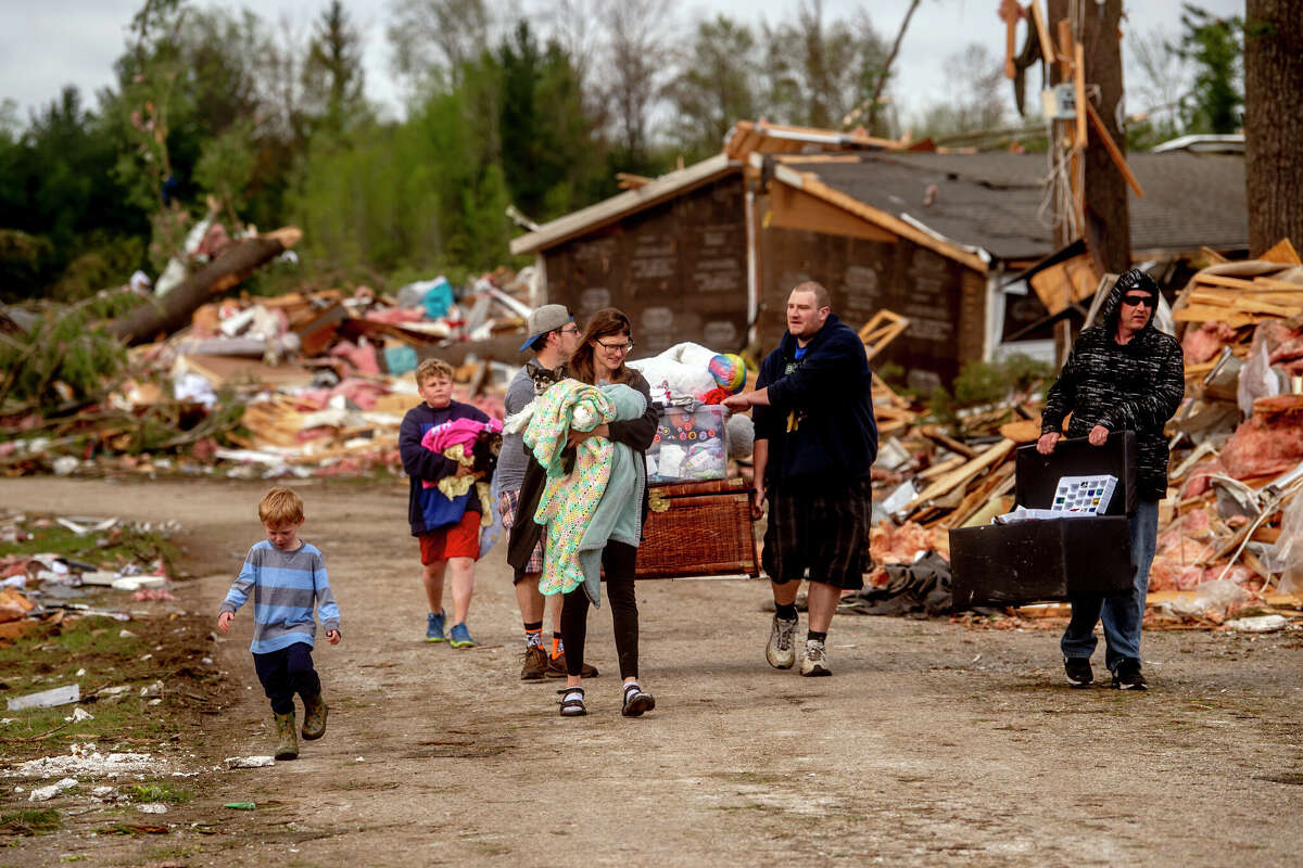Resident Stephanie Kerwin, center, holds her baby Octavius in one arm and dog Pixie in the other as she and her family carry what they could salvage from her home in Nottingham Forest Mobile Home Park, Saturday, May 21, 2022, in Gaylord, Mich., following a tornado the day before. "This morning is when it first hit me...I could have lost people that I really love. I am so grateful," Kerwin said. (Jake May/MLive.com/The Flint Journal via AP)