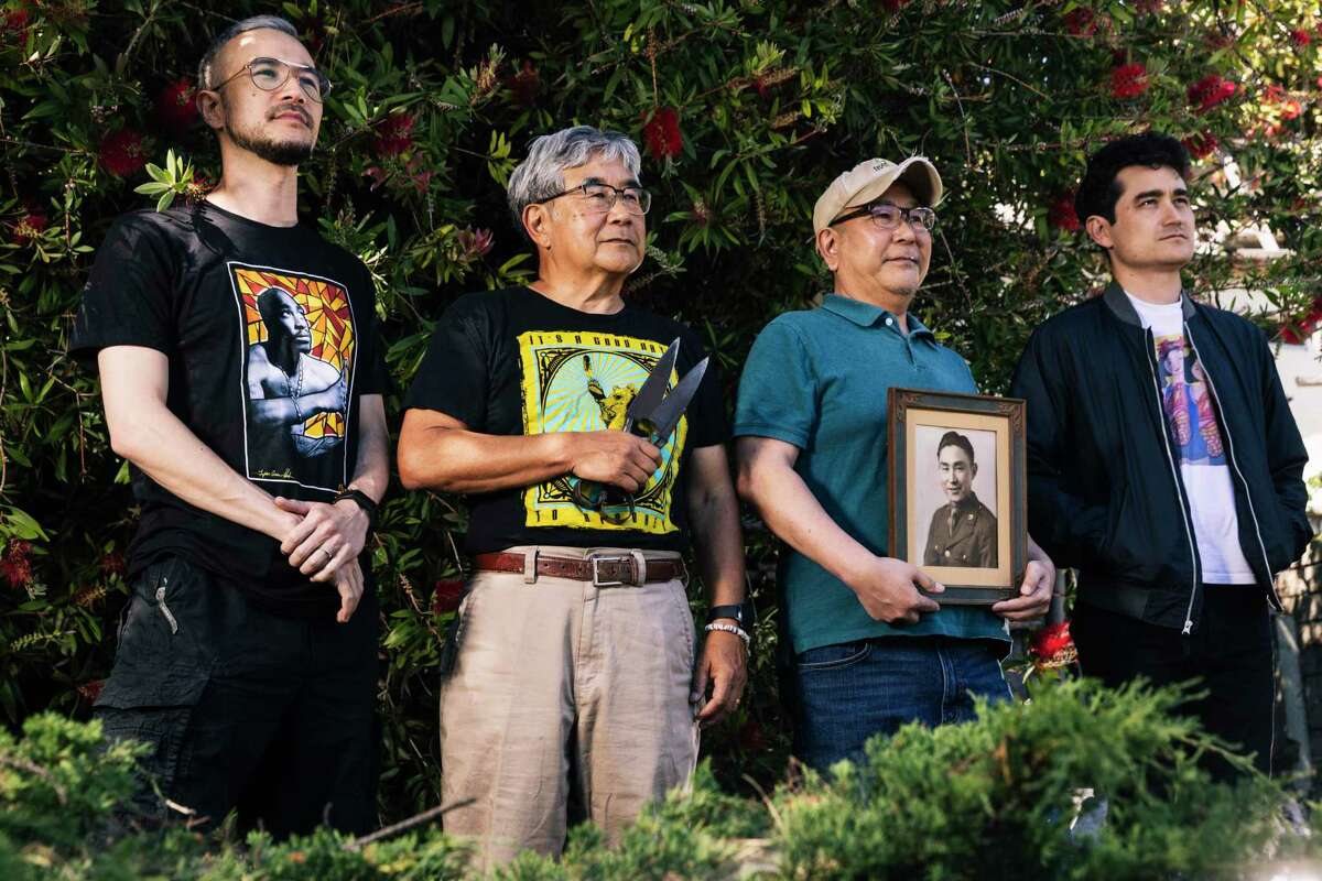 Flanked by sons Colin, left, and Aki, right, Paul Ehara, second left, holds a pair of steel sheep shears as his brother Richard, second from right, holds a photograph of their late father John in their family home garden cultivated by John in El Cerrito, Calif. Saturday, May 21, 2022. John, a second generation Japanese-American who was incarcerated in an internment camp during World War II and drafted to work as a translator in U.S. Army Intelligence in postwar Japan before returning stateside to start a gardening business, will be posthumously receiving a high school degree from Mount Diablo High School in Concord on Tuesday.