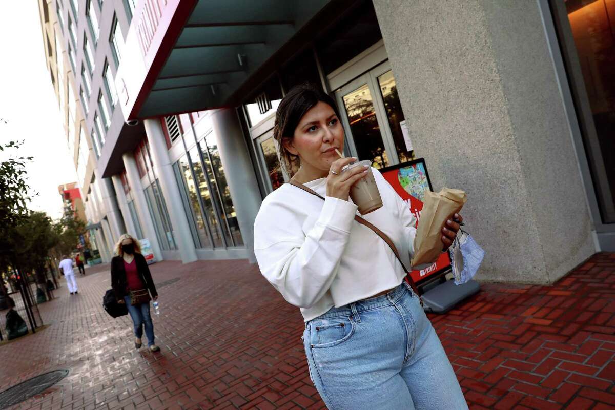 Kelsey Duff, a new resident of Trinity Place, sips her drink as she walks on Market Street in San Francisco. The apartment complex includes some rent-controlled units.