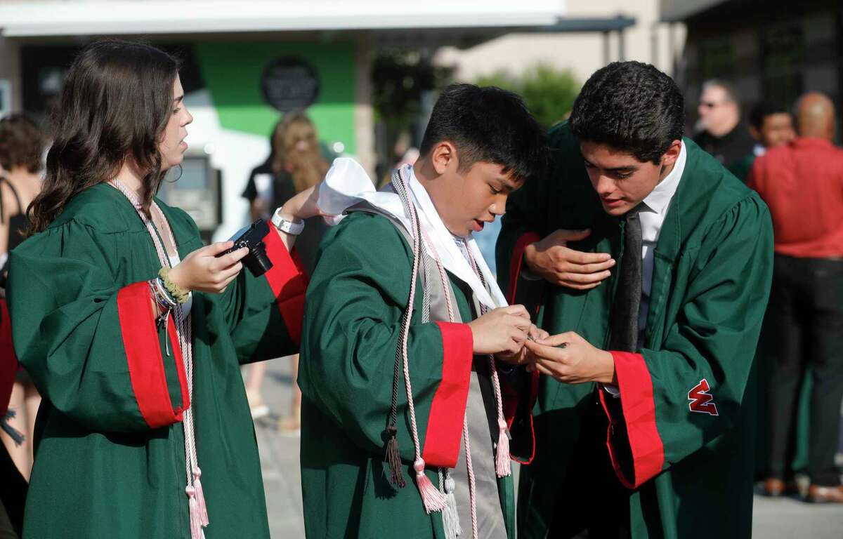 The Woodlands High School senior Makayla Mott, left, and Santiago Padilla, right, helps Matt Limsiaco with his graduation attire before a graduation ceremony at Cynthia Woods Mitchell Pavilion, Monday, May 23, 2022, in The Woodlands.