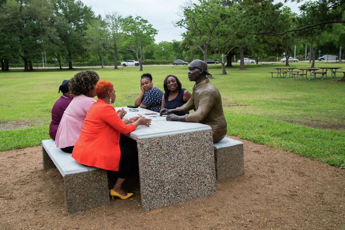 Dannette Davis, center, whose foundation donated statue to Harris County sit by a sculpture depicting George Floyd smiles as she looks at the sculpture seated at an outdoor table welcoming everyone to have a seat and join him, Tuesday, May 24, 2022, in Houston. Created by renowned sculptor Adrienne Rison-Isom, the statue was donated to Harris County by Dannette Davis of Kay Davis Associates.