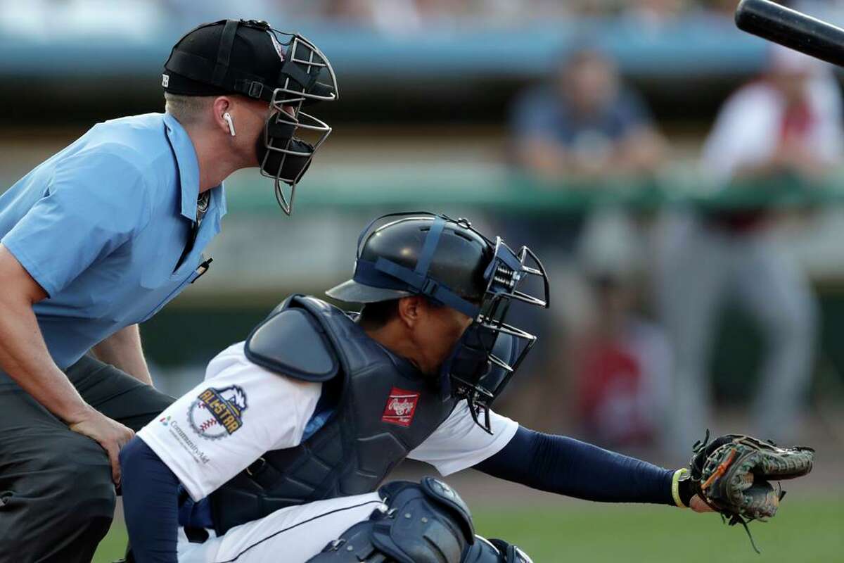 Home plate umpire Brian deBrauwere, left, huddles behind Freedom Division catcher James Skelton, of the York Revolution, as the official wears an earpiece during the first inning of the Atlantic League All-Star minor league baseball game, Wednesday, July 10, 2019, in York, Pa. deBrauwere wore the earpiece connected to an iPhone in his ball bag which relayed ball and strike calls upon receiving it from a TrackMan computer system that uses Doppler radar. The independent Atlantic League became the first American professional baseball league to let the computer call balls and strikes during the all star game. (AP Photo/Julio Cortez)