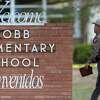 A state trooper walks Tuesday, May 24, 2022 past the Robb Elementary School sign in Uvalde, Texas the day a gunman entered the school and killed at least 18 children and three adults.