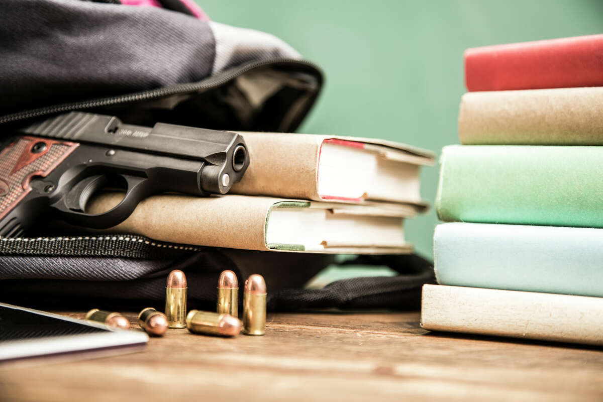 Gun violence in school setting. Scene shows gun, bullets and books inside high school student's backpack with book stack and cell phone. Items lie on school desk with chalkboard background. School violence remains an important topic in today's society.