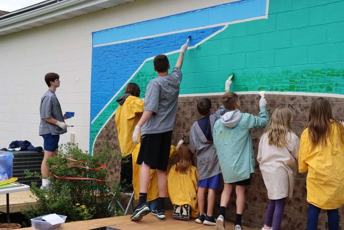 Students from Onekama Consolidated Schools apply texture to a garden mural being painted on the Farr Center in Onekama.