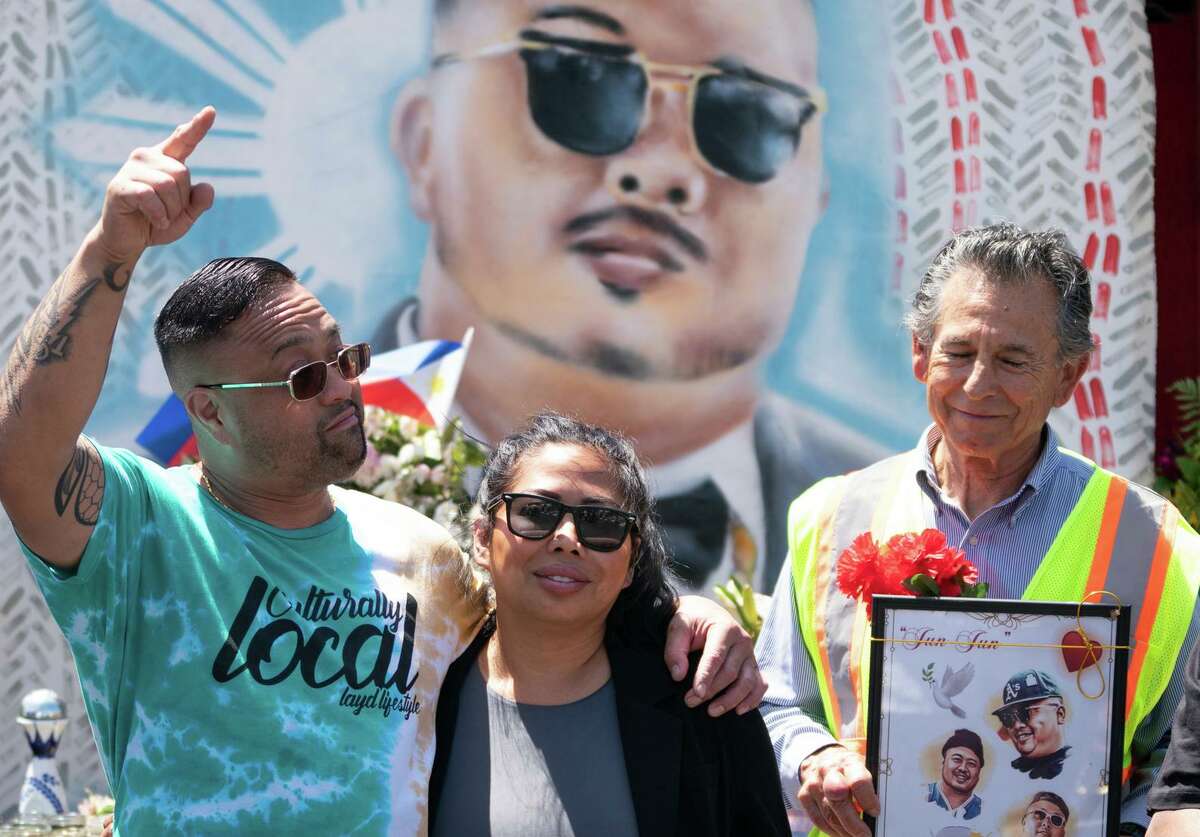 Mark Legaspi, cousin of Artgel “Jun” Anabo, embraces Anabo’s sister, Analyn Novenario (center), while Council Member Noel Gallo holds pictures of the late restaurateur during a news conference Wednesday addressing his killing at Lucky Three Seven restaurant in Oakland.