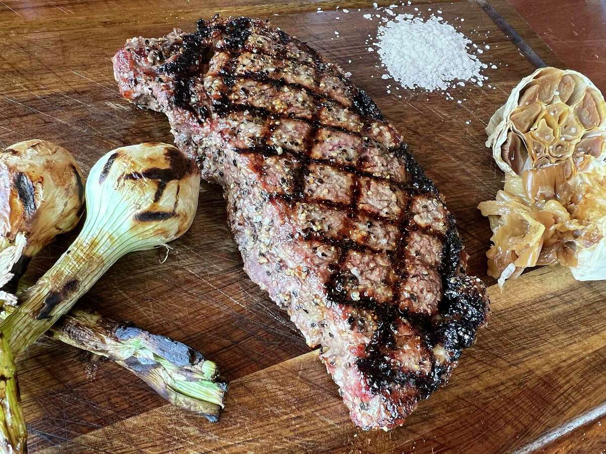 A 12-ounce New York strip steak comes with grilled onions and roasted garlic at Tu Asador, a Mexican-style steakhouse in Castle Hills.
